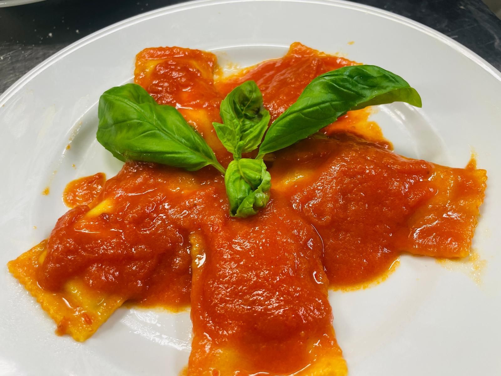 Ravioli al sugo di pomodoro guarniti con basilico su un piatto bianco.