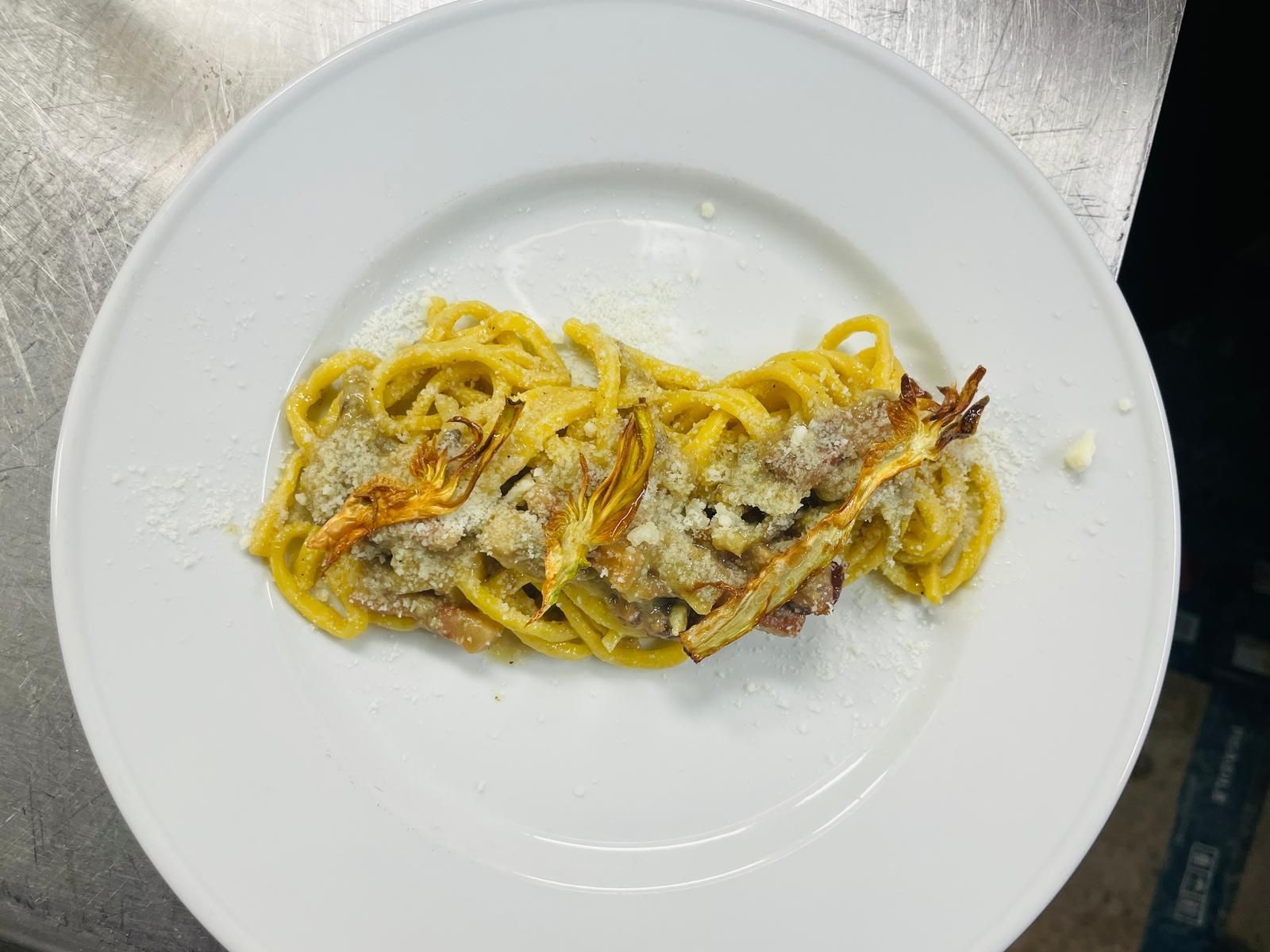 Piatto di pasta con tagliatelle gialle, formaggio e verdure su un piatto bianco.