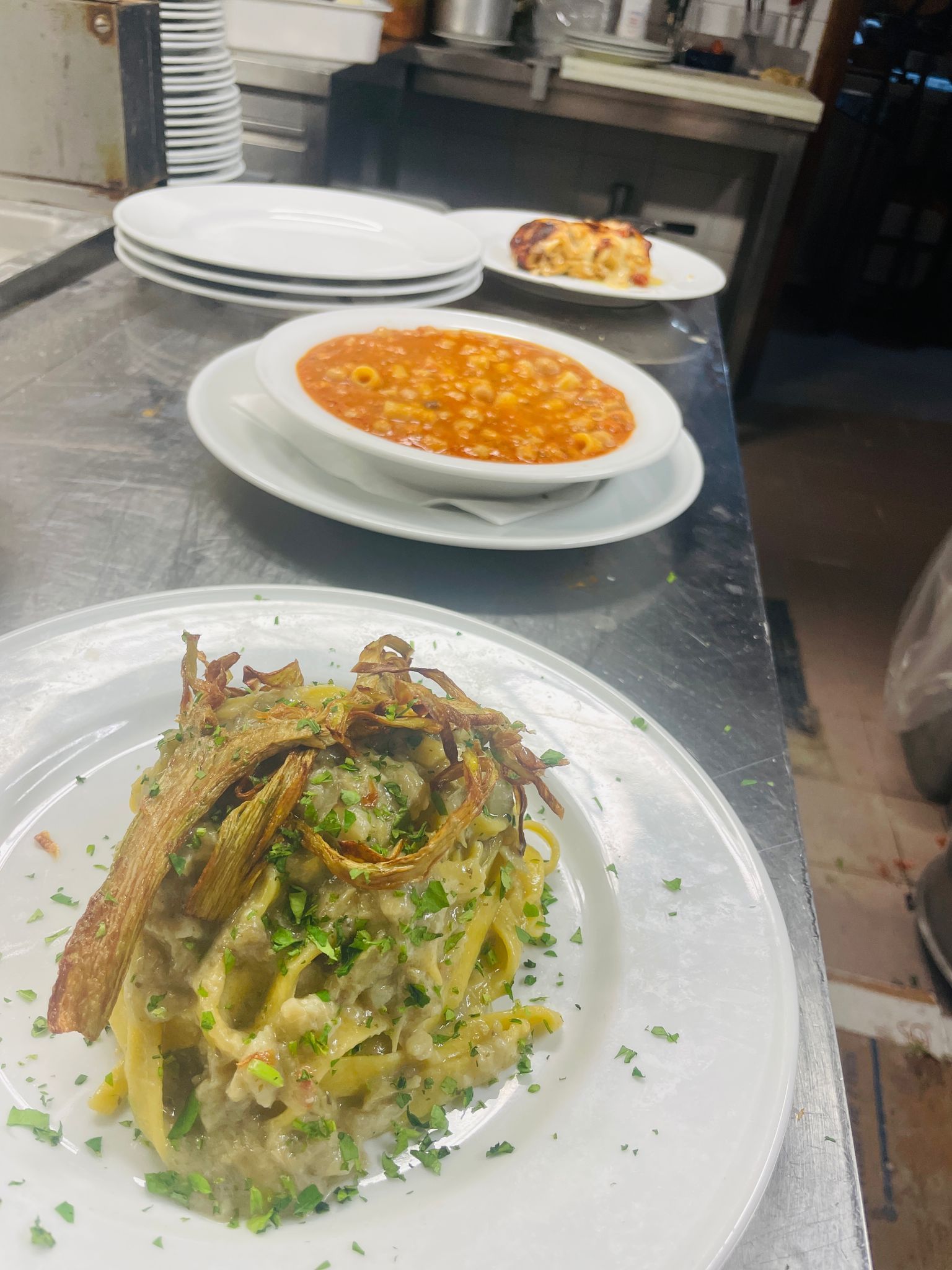 Piatto di pasta con condimenti croccanti, servito insieme ad altri piatti sul piano di lavoro della cucina.
