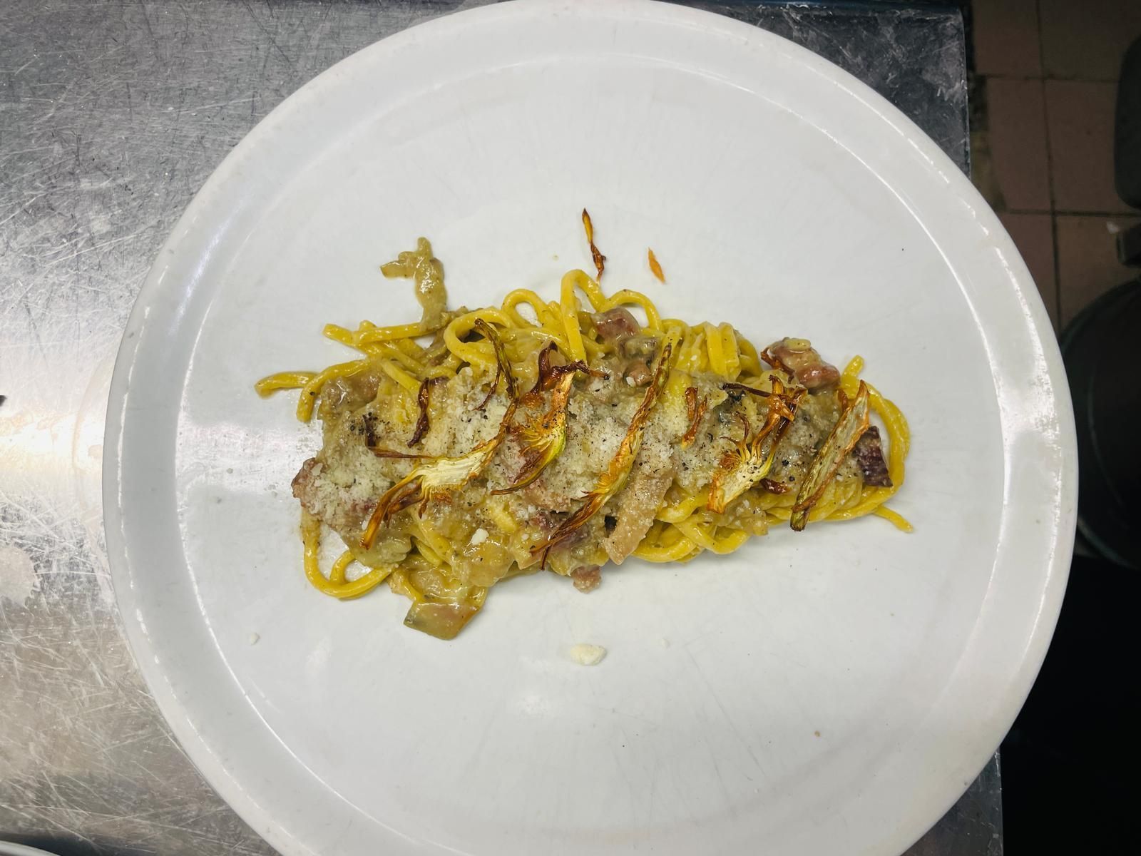 Piatto di pasta su un piatto bianco, con tagliatelle gialle, carne e condimento.