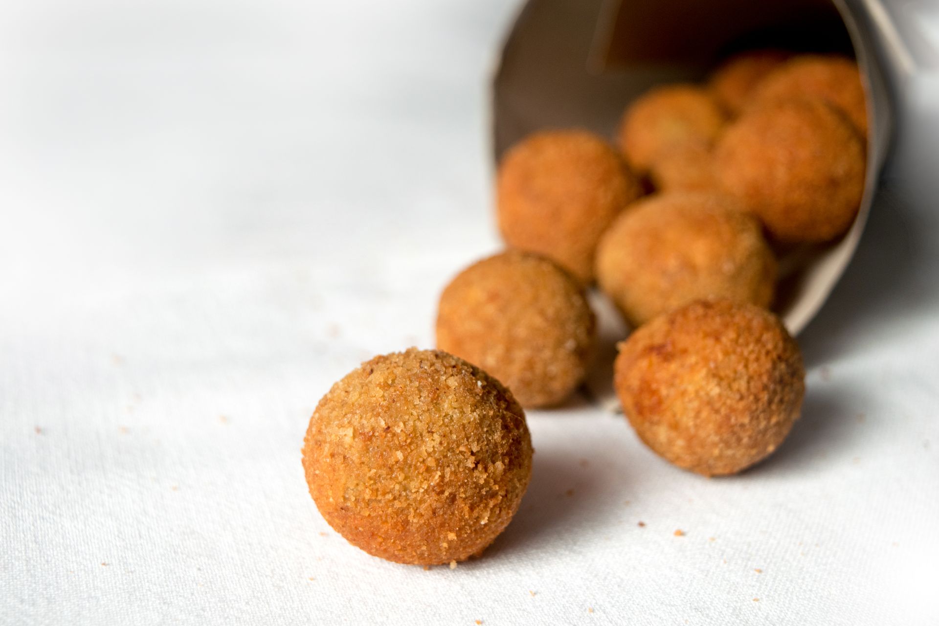 Palline di cibo fritte e dorate che cadono da un cono di carta su una superficie bianca.