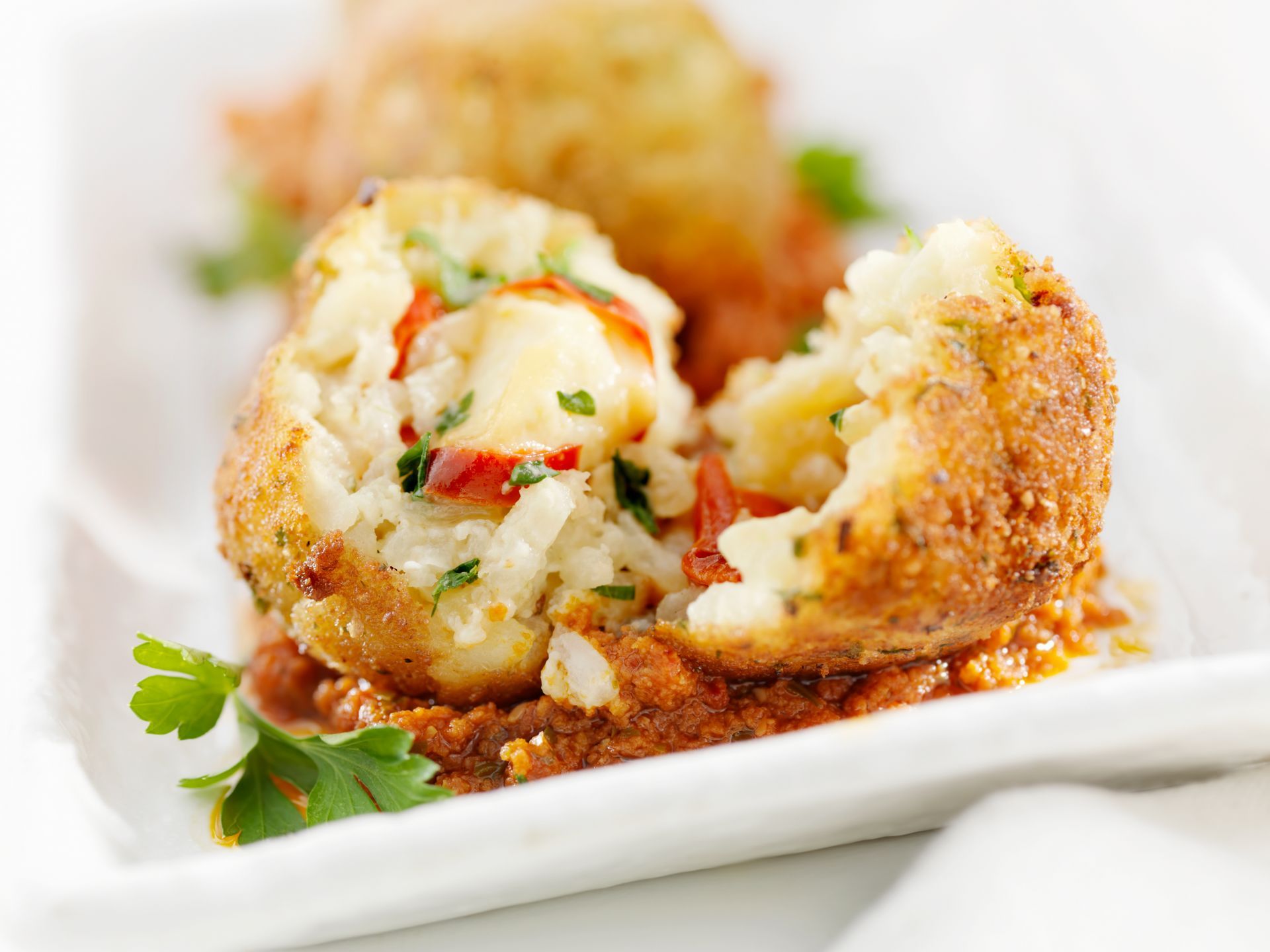 Primo piano di una palla di arancino tagliata a metà, che rivela riso, mozzarella e pomodoro su un piatto con salsa rossa.
