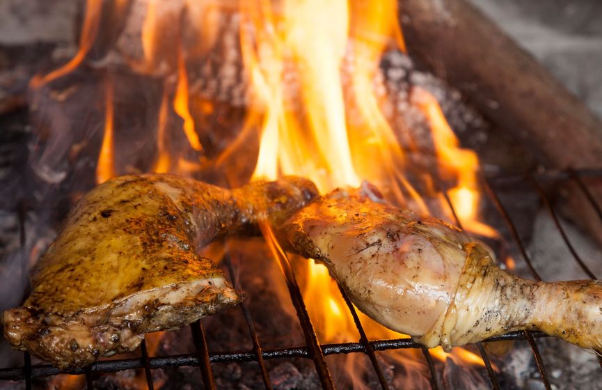 Cosce di pollo grigliate sul fuoco, con le fiamme visibili.
