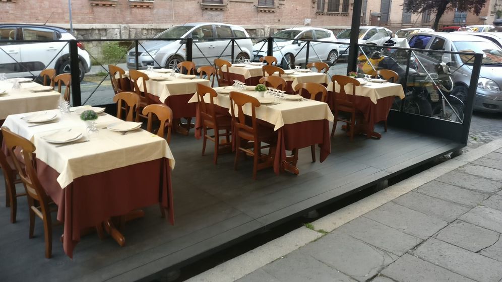 Posti a sedere all'aperto su una piattaforma rialzata, tavoli con tovaglie color crema e gonne marroni, sedie, auto parcheggiate sullo sfondo.