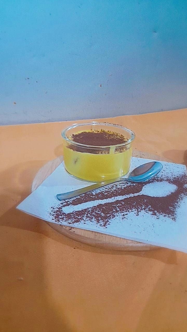 Dolce giallo in un bicchiere, spolverato con cacao in polvere, servito su un tovagliolo.