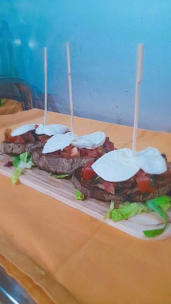Tre antipasti di bruschette con mozzarella, pomodori e basilico su un tagliere di legno.