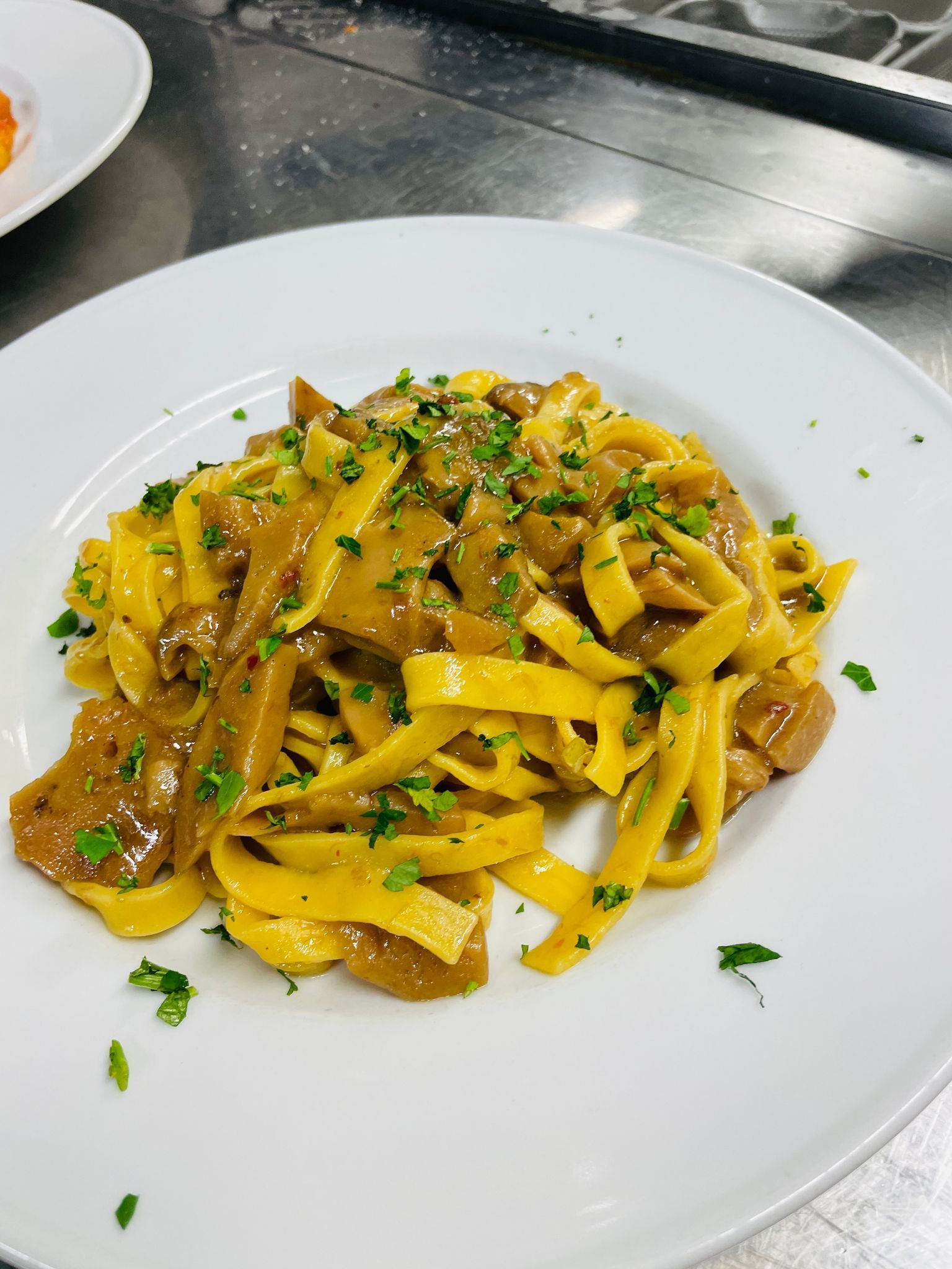 Fettuccine con sugo ai funghi, guarnite con prezzemolo, su un piatto bianco.