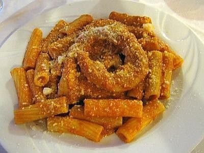 Piatto di pasta con rigatoni e anelli di cipolla fritti su un piatto bianco, conditi con formaggio grattugiato.