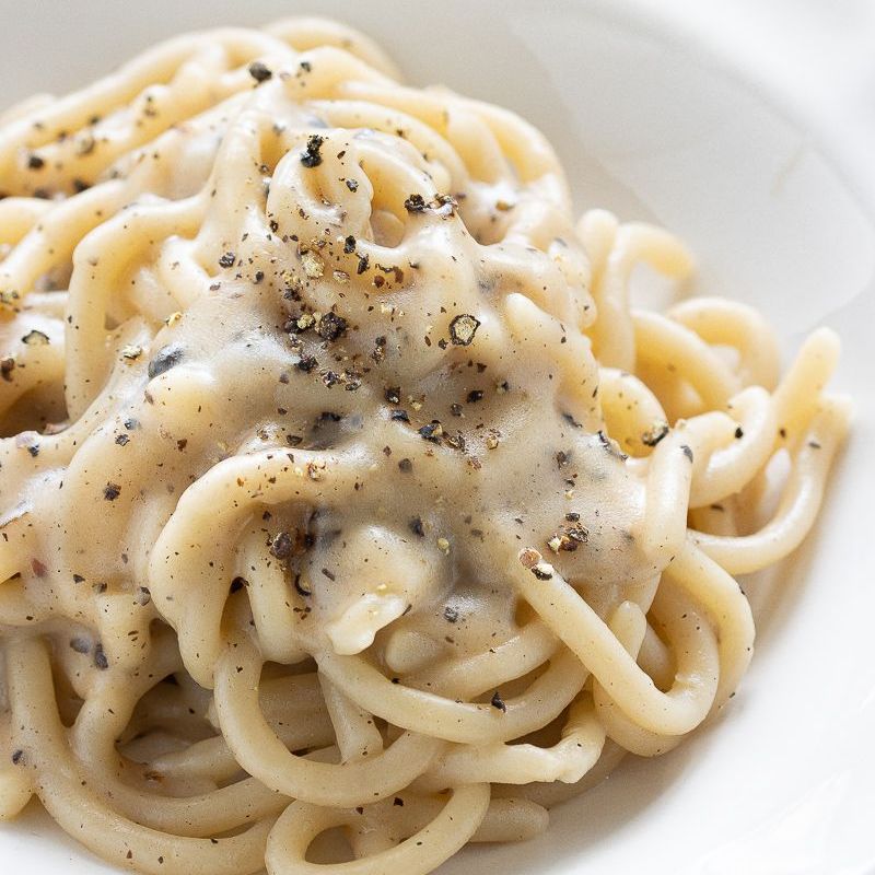 Pasta in salsa bianca cremosa, cosparsa di pepe nero, in una ciotola bianca.