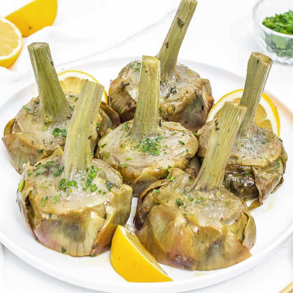 Carciofi al vapore su un piatto bianco con spicchi di limone.