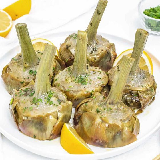 Carciofi al vapore su un piatto bianco con spicchi di limone.