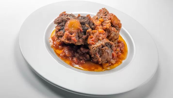 Carne brasata con salsa di pomodoro su un piatto bianco.
