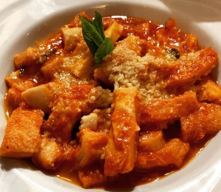 Piatto di trippa in salsa rossa, guarnito con formaggio grattugiato e rametto di menta.