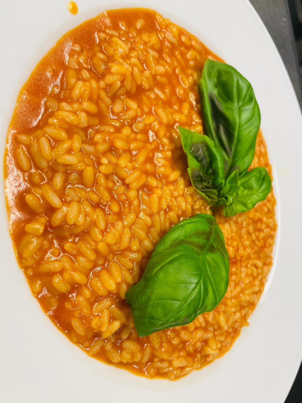 Risotto al pomodoro con foglie di basilico fresco su un piatto bianco.