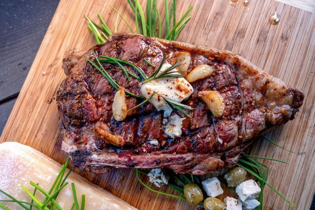 Bistecca alla griglia su un tagliere di legno con aglio, rosmarino e formaggio.