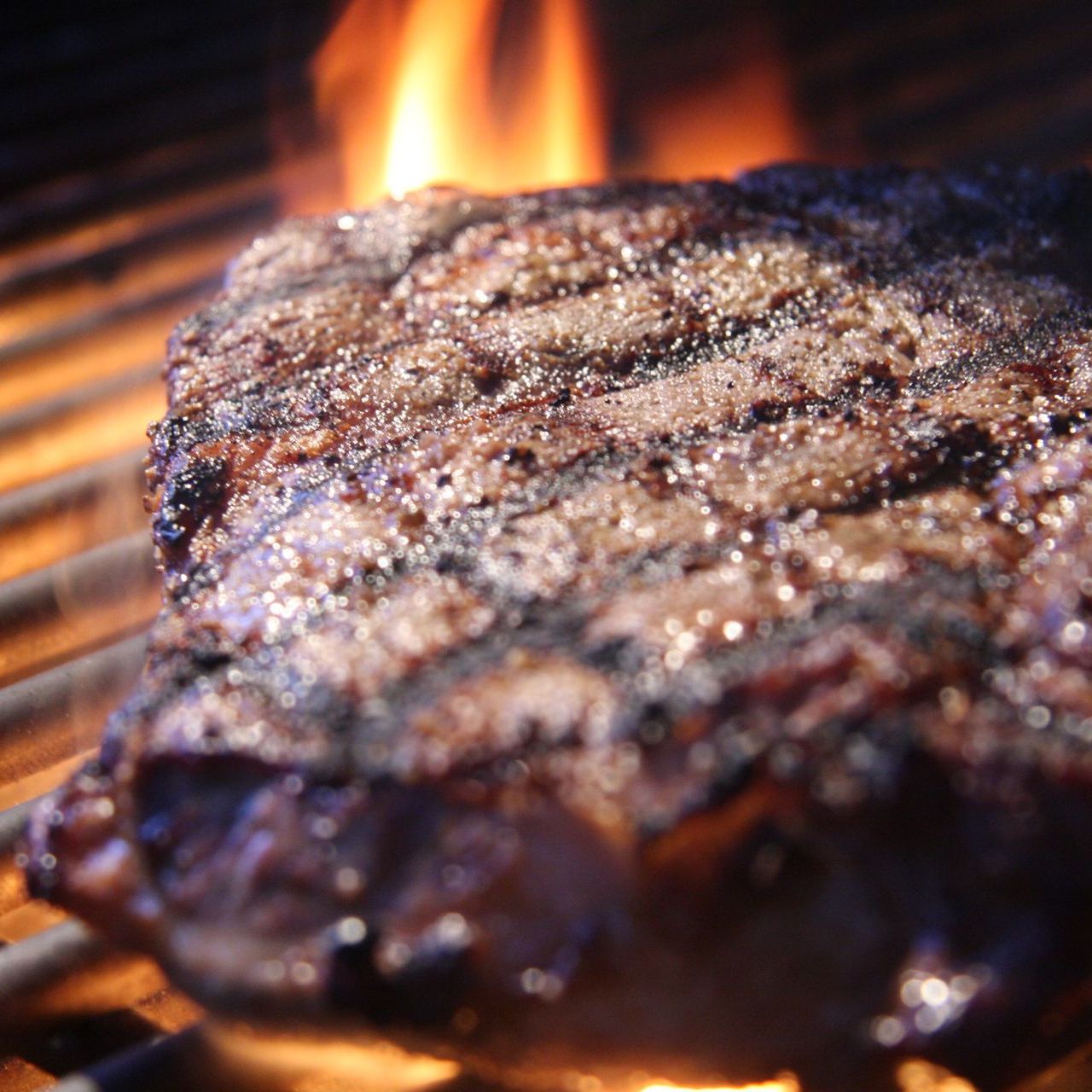 Bistecca alla griglia con fiamme, che mostra i segni della griglia e la superficie lucida.