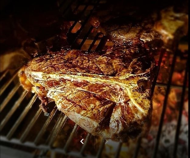 Una grande bistecca cotta su una griglia di metallo sopra carboni ardenti.