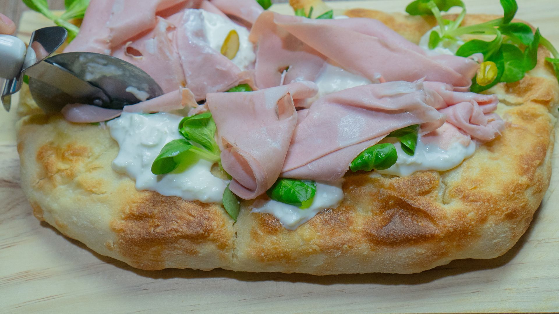 Pane piatto condito con formaggio bianco, prosciutto, verdure e olive nere.