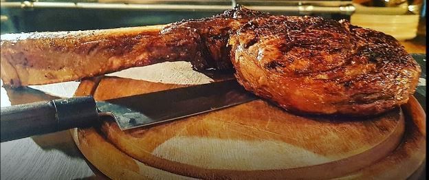 Una grande bistecca tomahawk su un tagliere di legno con un coltello.
