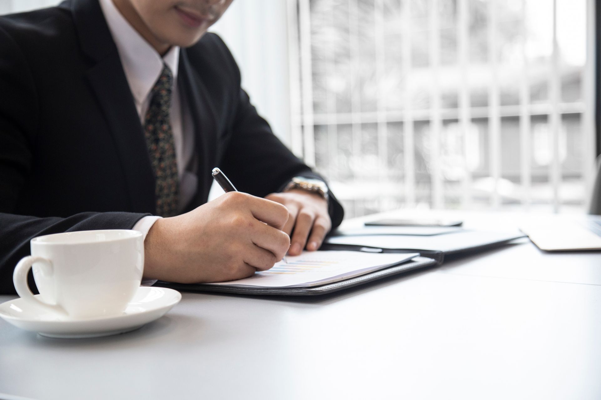 A man in a suit and tie is sitting at a table writing on a clipboard.
