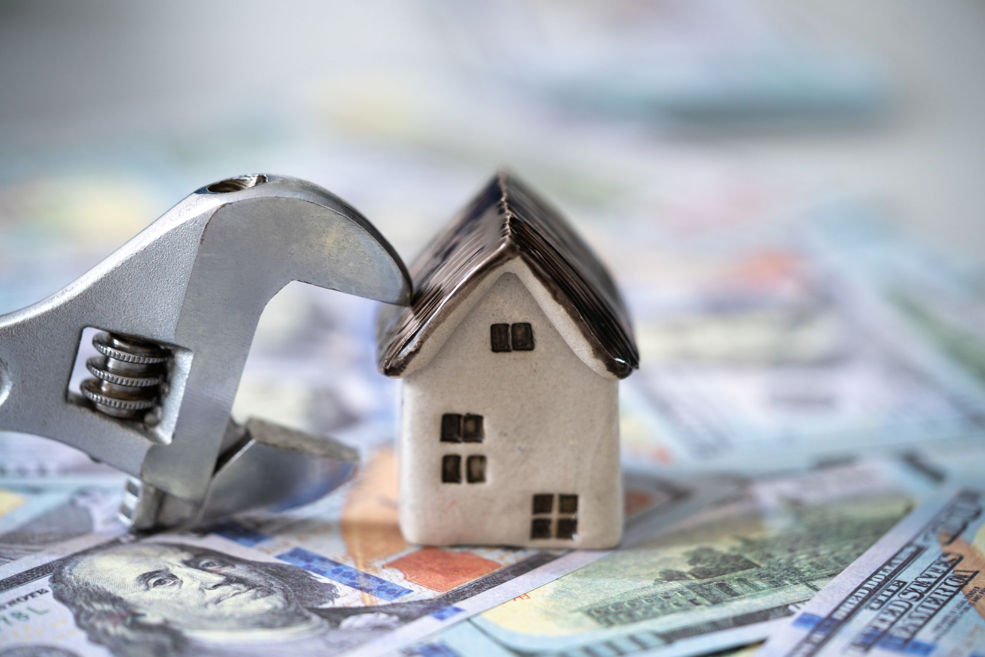 A wrench is holding a small house on top of a pile of money. A wrench is holding a small house on top of a pile of money.