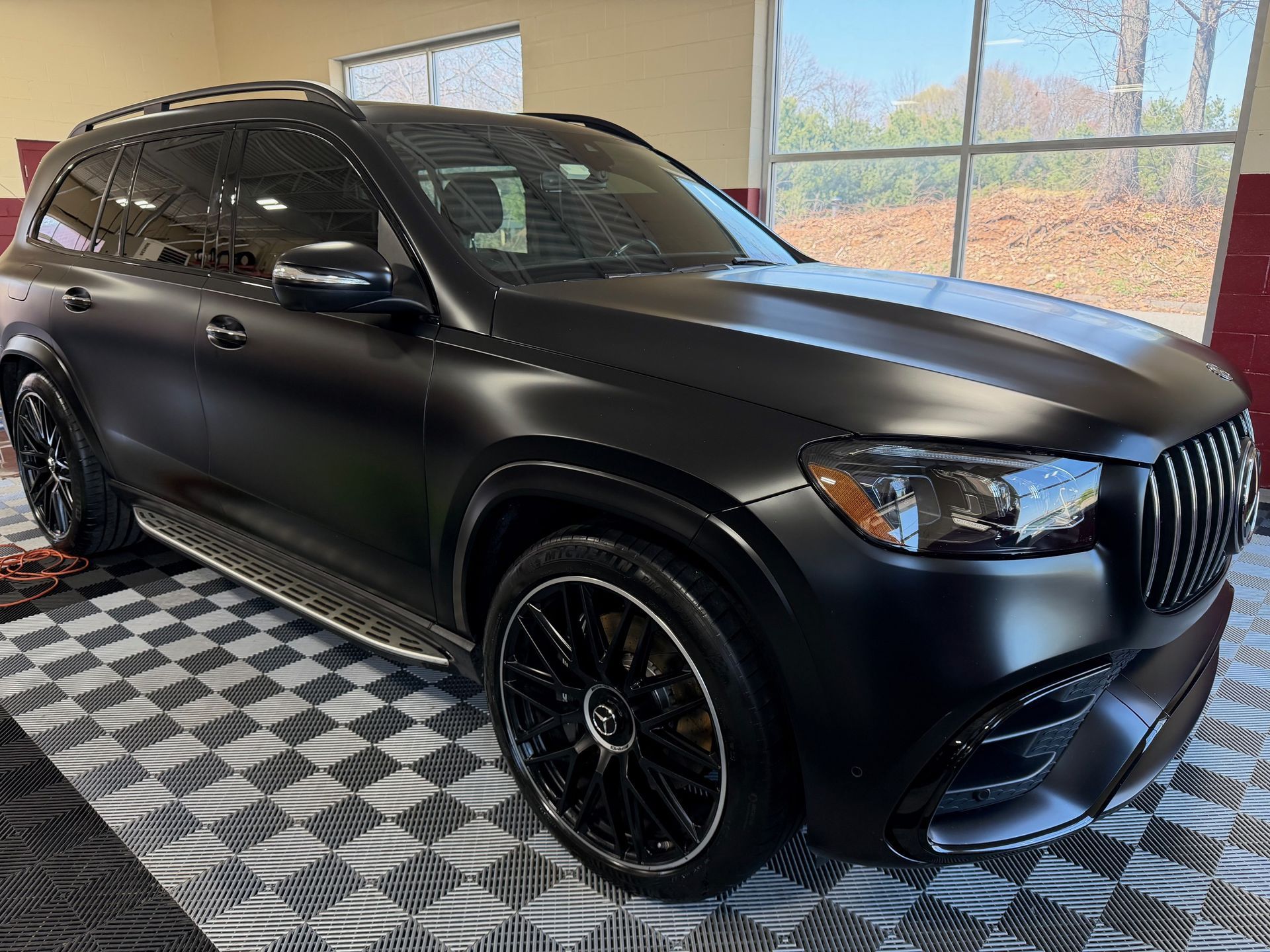 Matte black SUV parked indoors on a checkered floor near large windows
