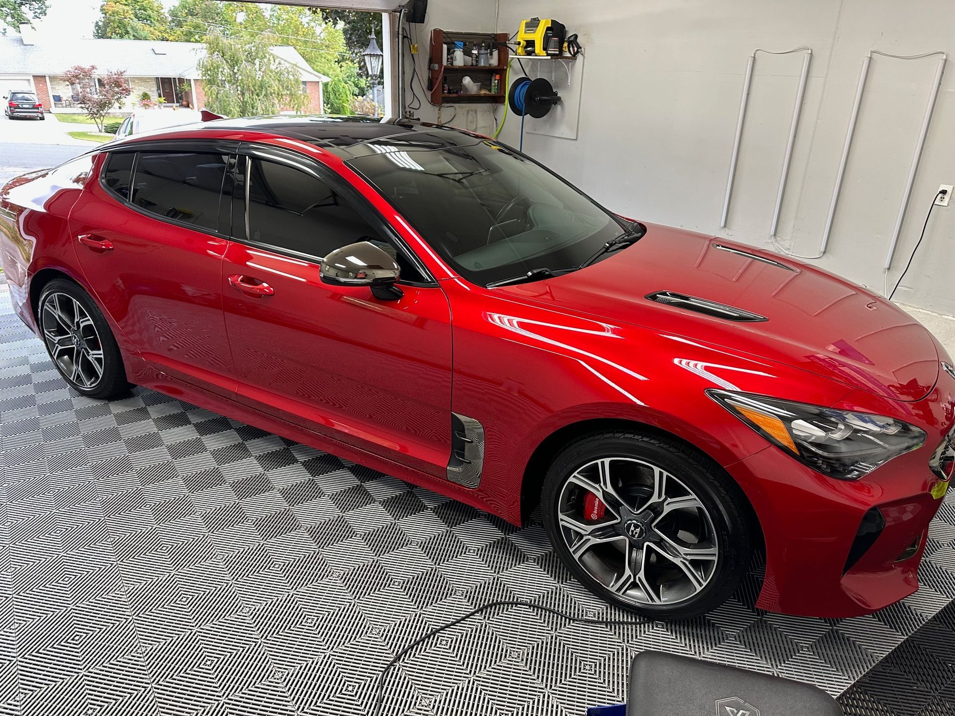 Red Kia Stinger car parked inside a garage with black and white flooring.