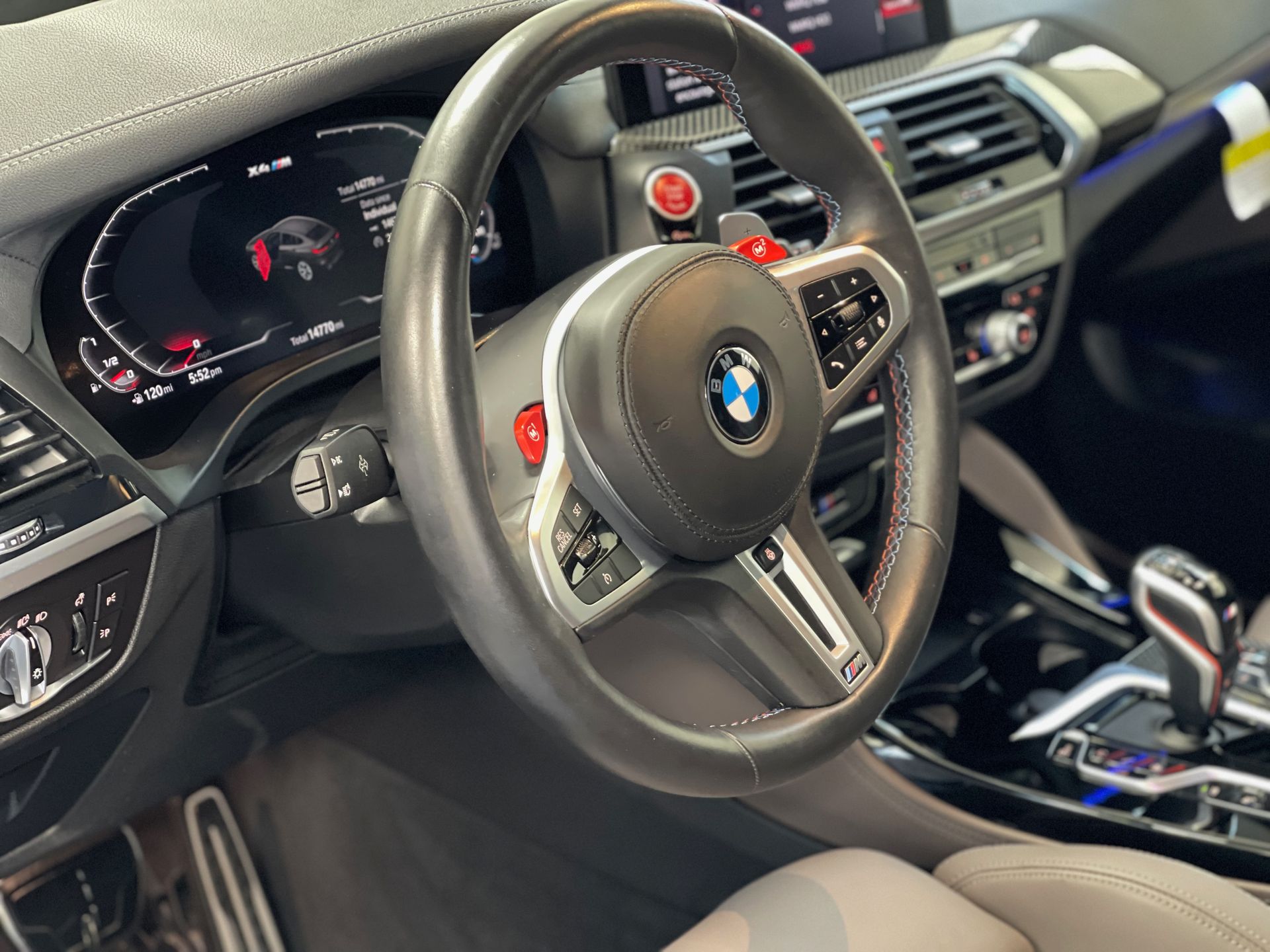 BMW X3 M interior with steering wheel and dashboard details. Red accents, black leather, digital display.