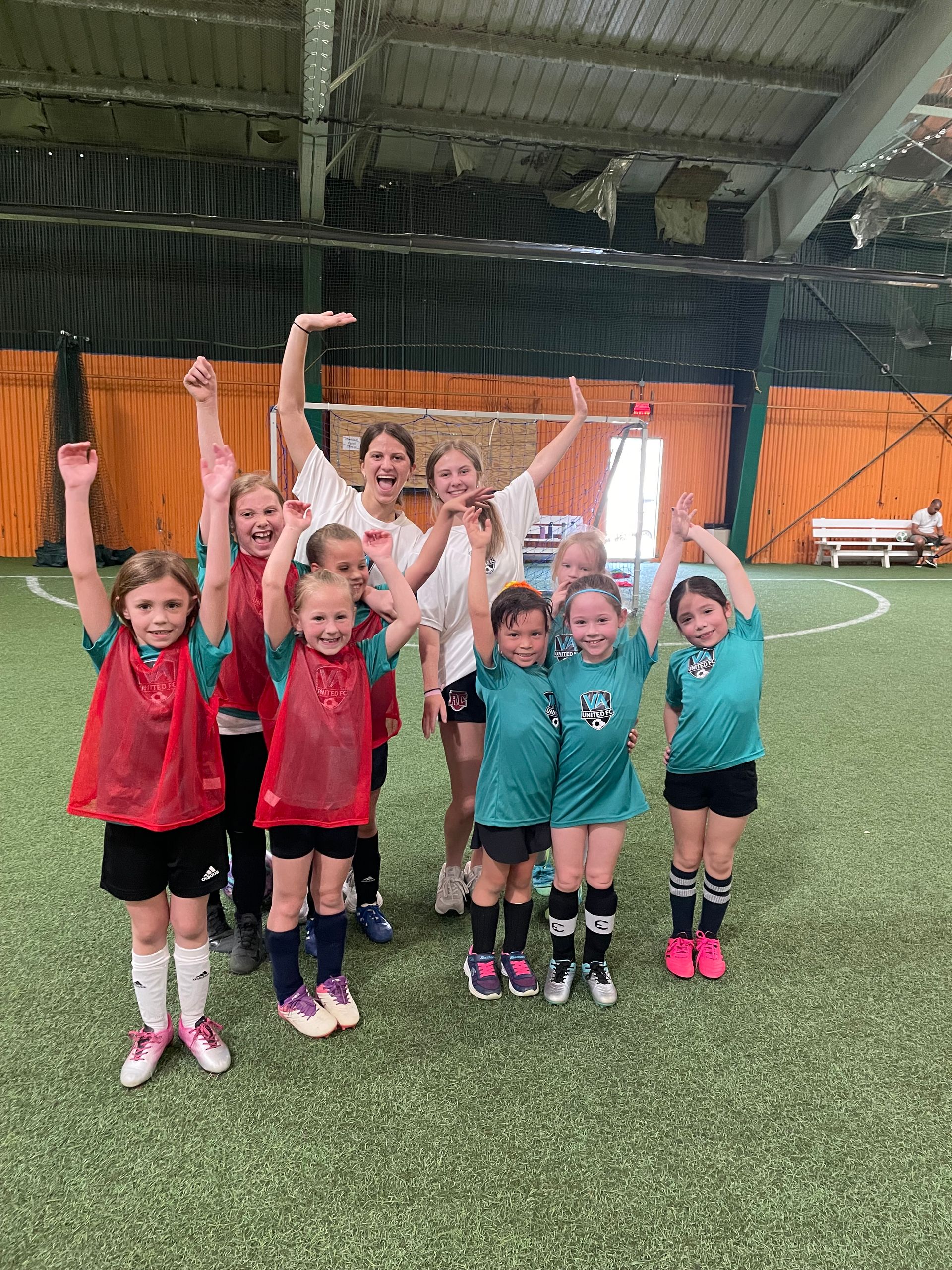 Youth soccer team cheering with arms raised on indoor turf field.
