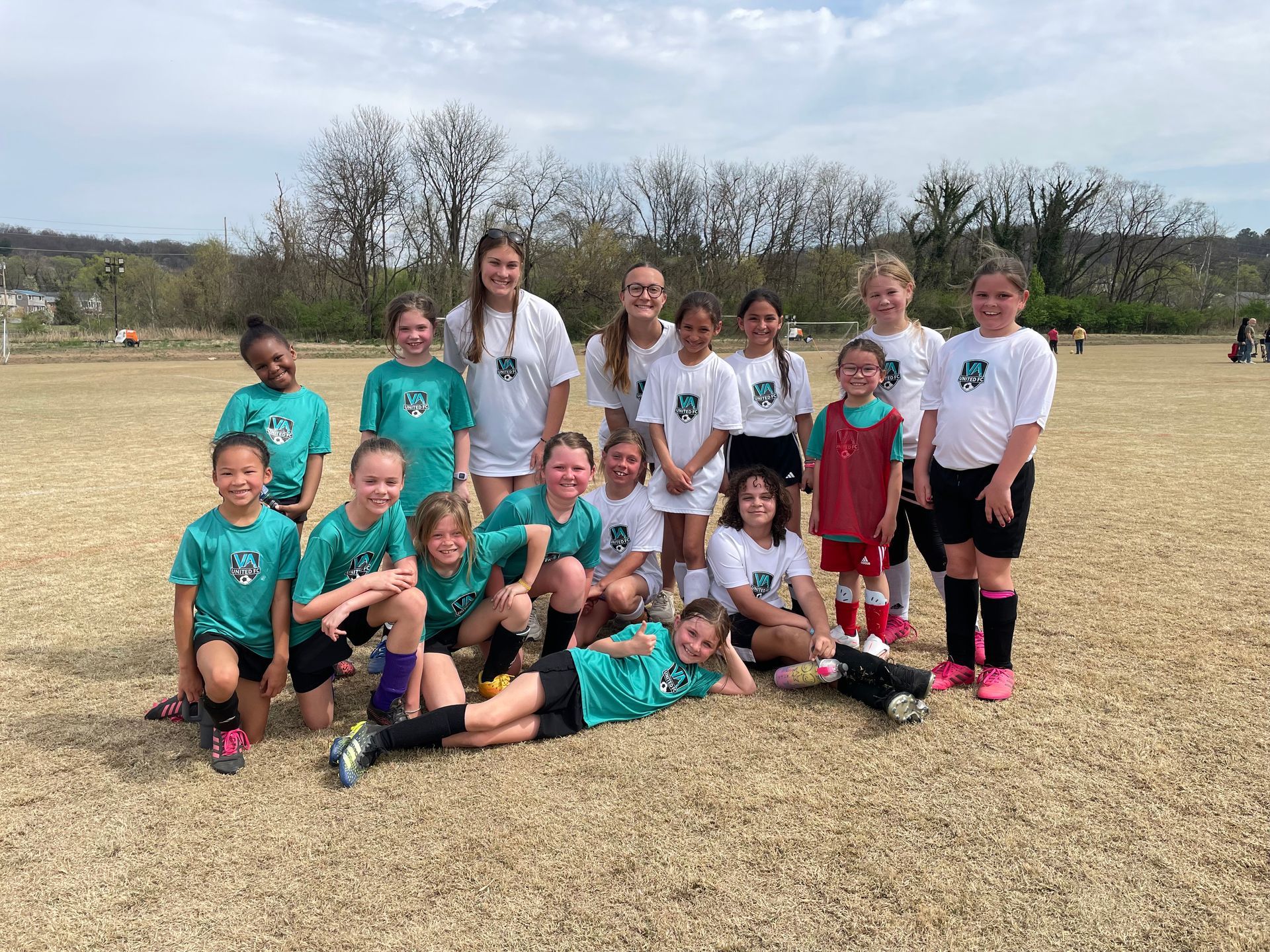 Youth soccer team posing on a field in matching teal and white uniforms.