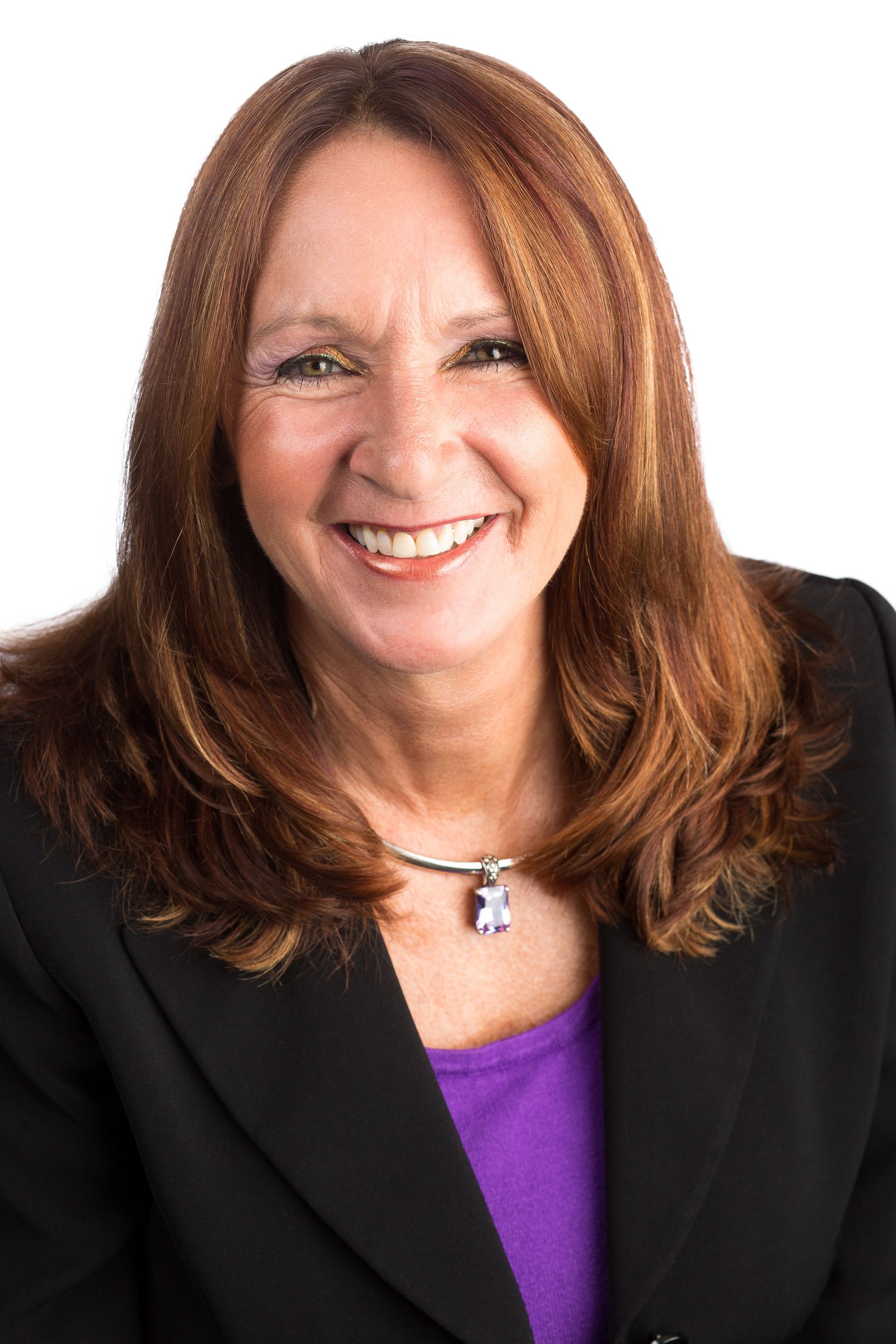 A woman wearing a black jacket and a purple shirt is smiling.