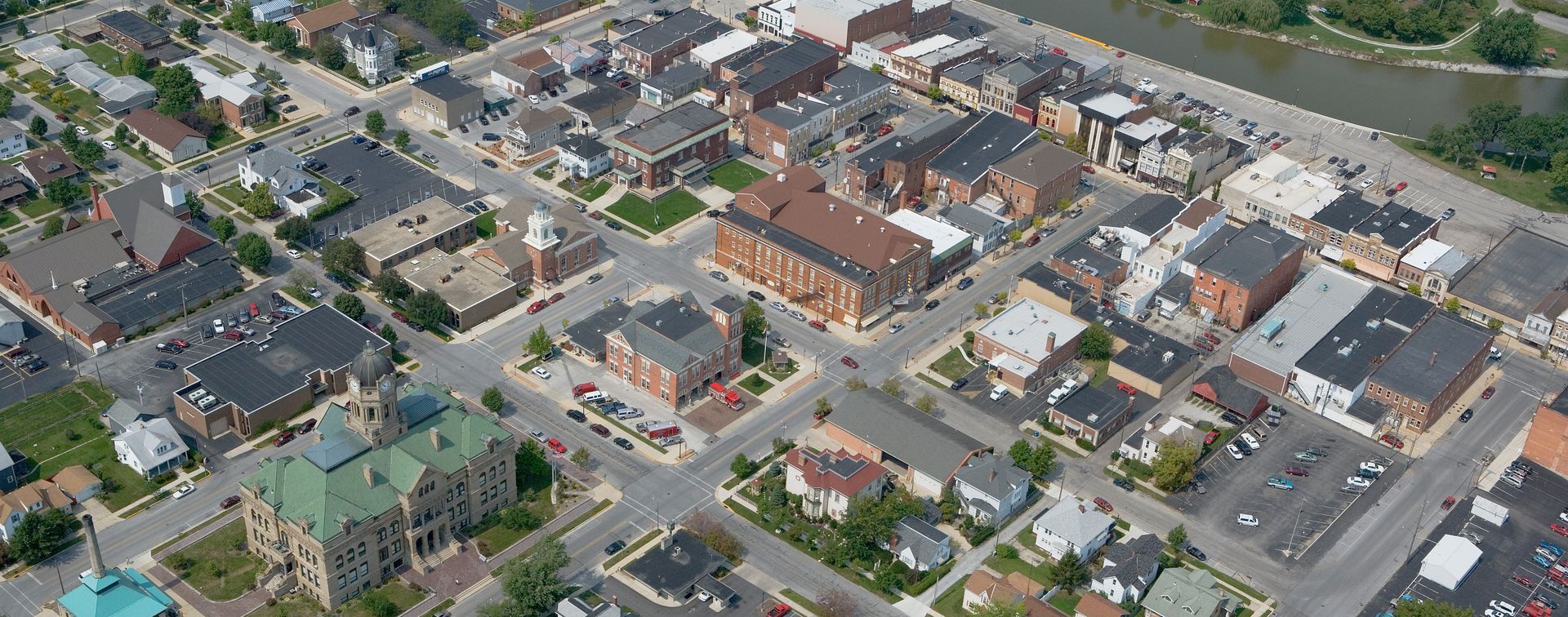 Aerial view of a town with buildings, streets, and green spaces. River on the right side of the image.