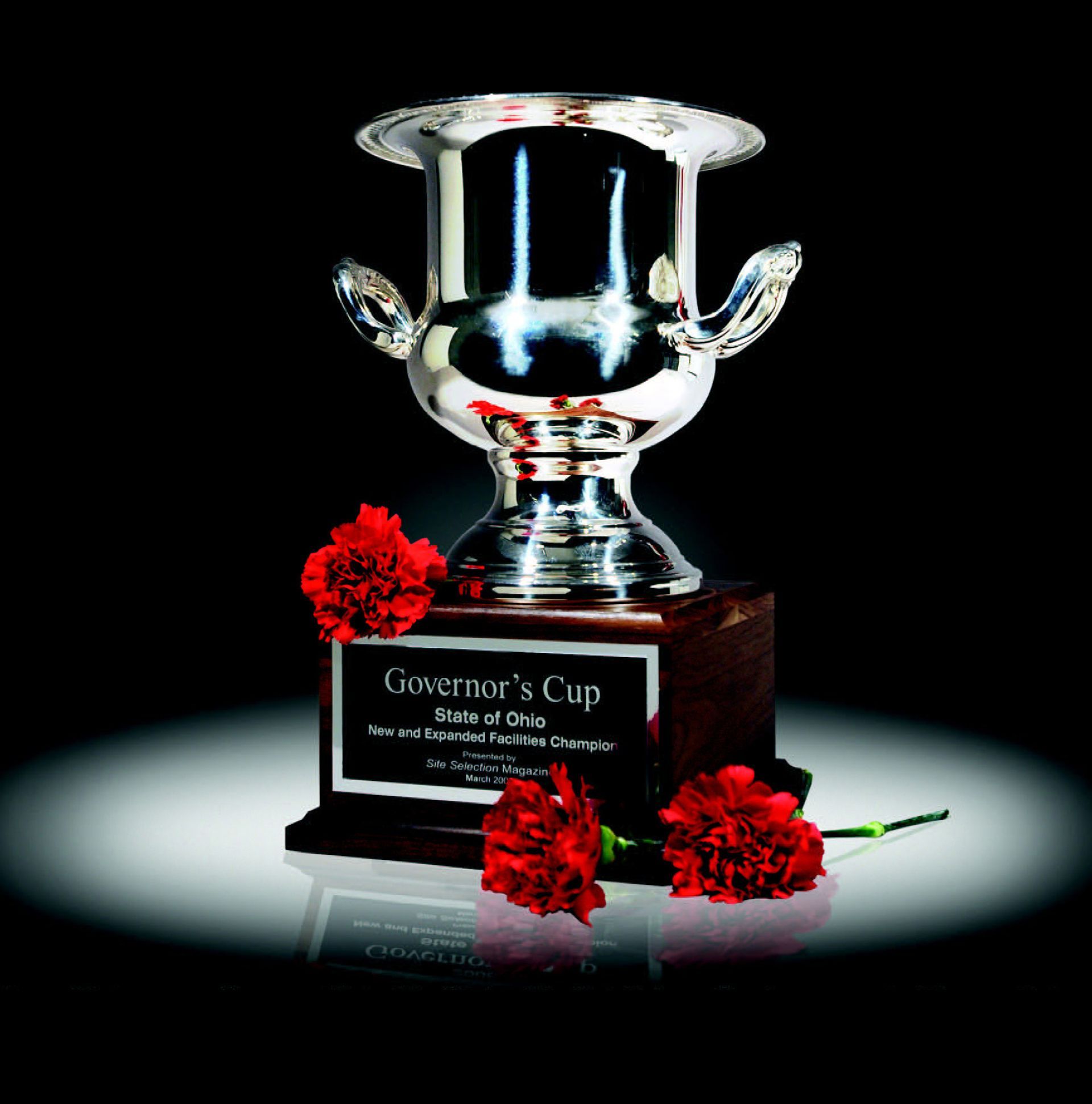 Silver Governor's Cup trophy with red carnations on a dark, reflective surface.