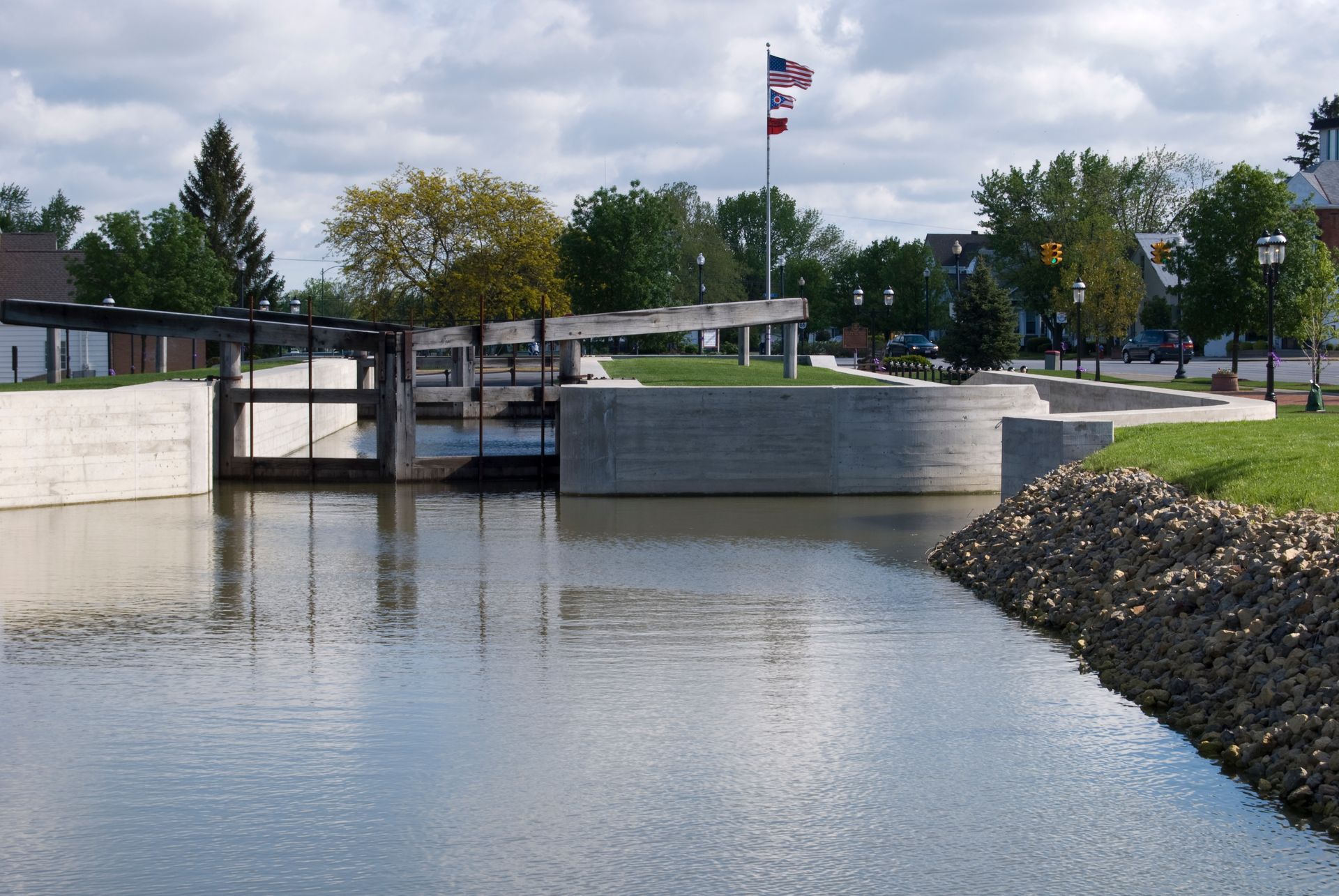 Canal with concrete walls, water lock, and American flag on a cloudy day.