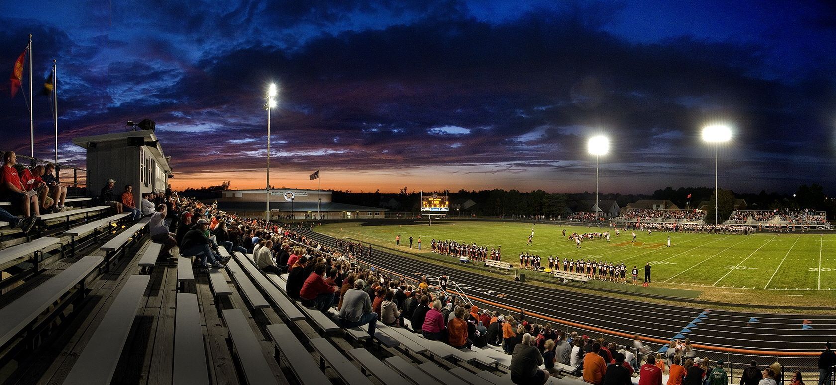 A football stadium filled with spectators under a twilight sky, stadium lights illuminated.