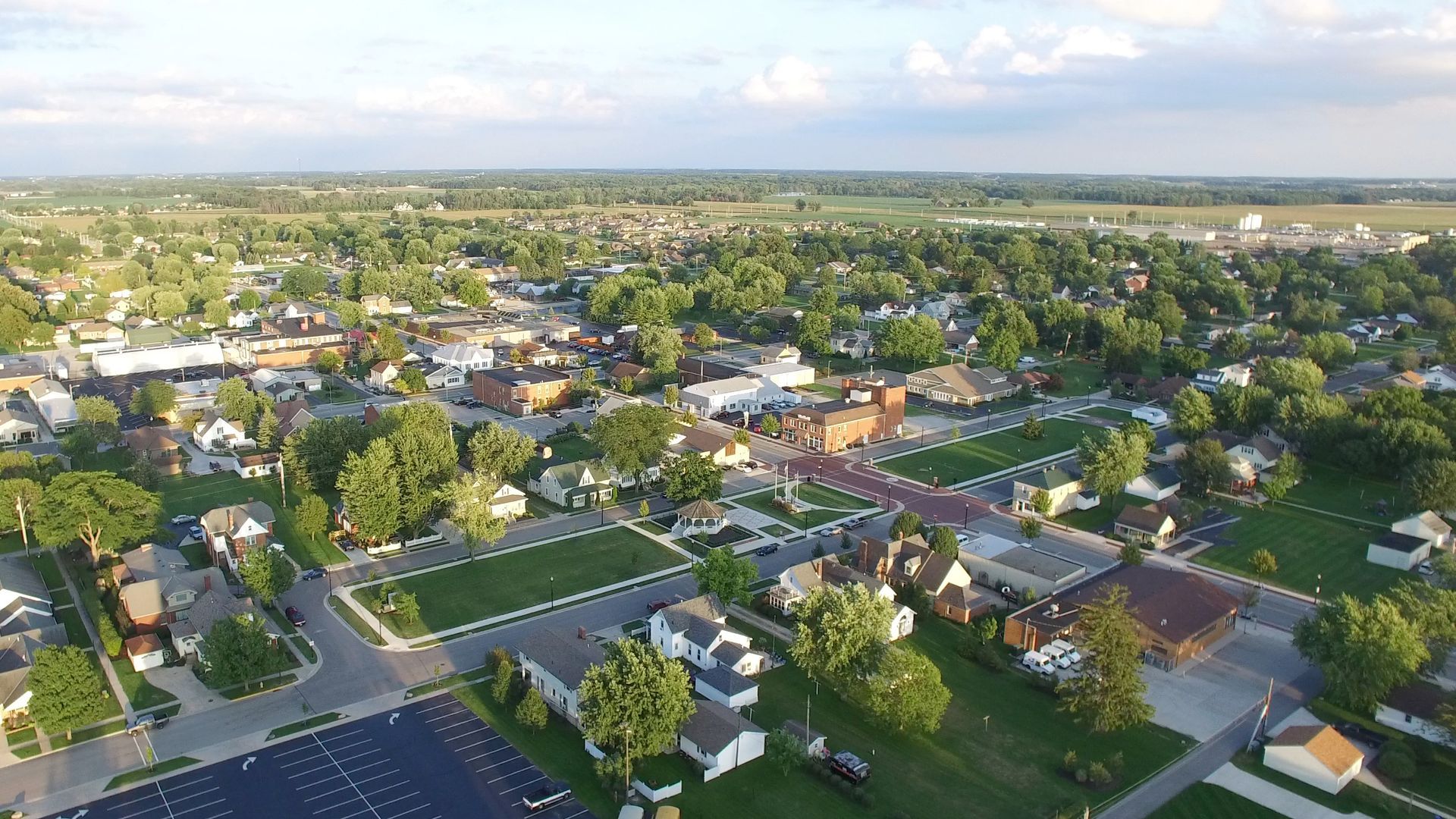 Aerial view of a small town with residential areas, buildings, and green spaces under a cloudy sky.