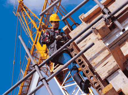 Construction worker on scaffolding, blue jeans, yellow hard hat, working near a crane.