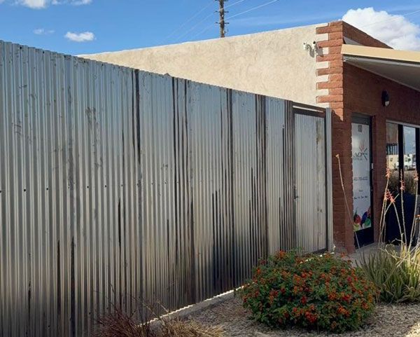 Corrugated metal fence beside a brick building with a shrub in front