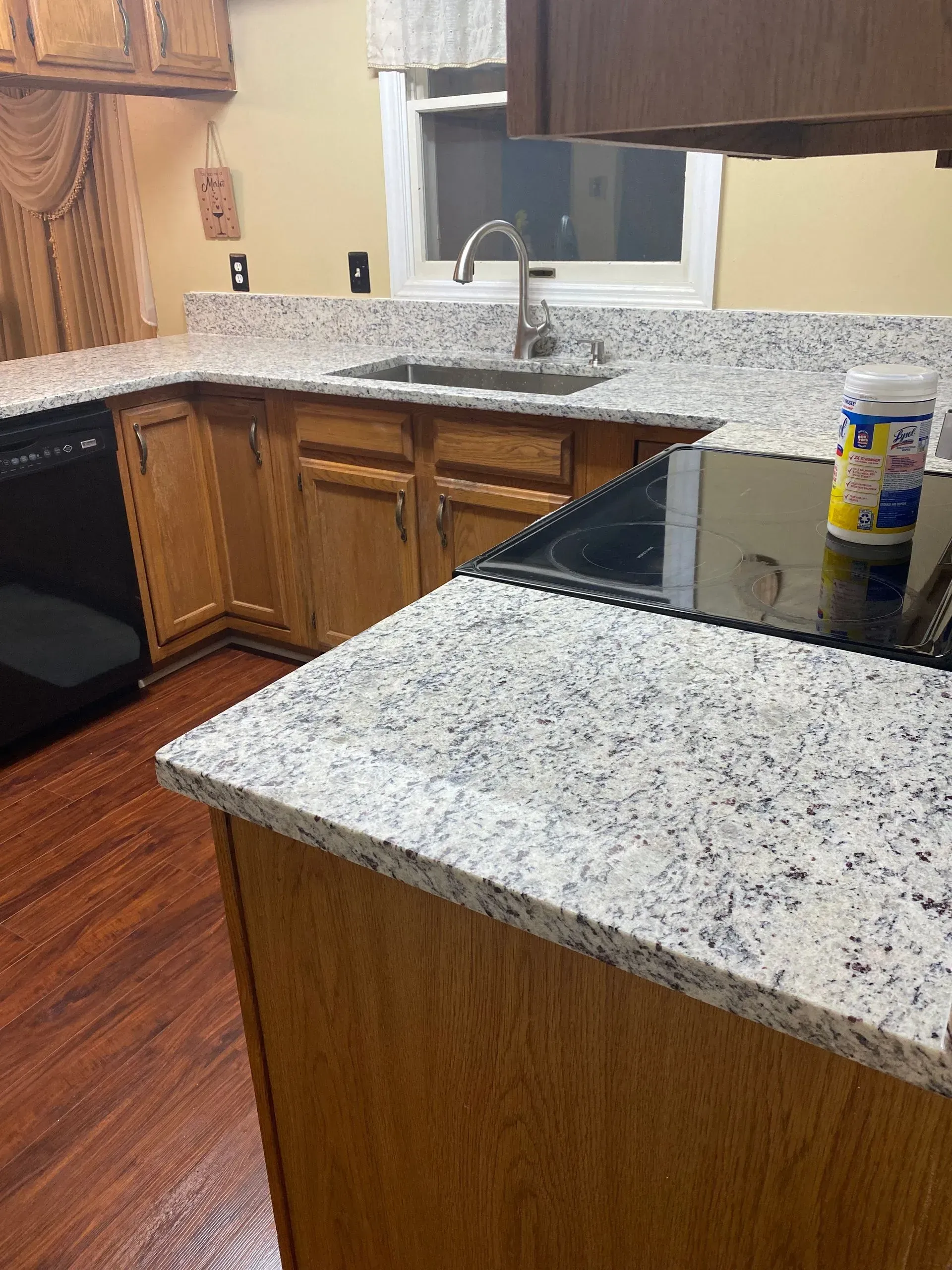 Kitchen with granite countertops, wooden cabinets, stainless sink, and a black stovetop.