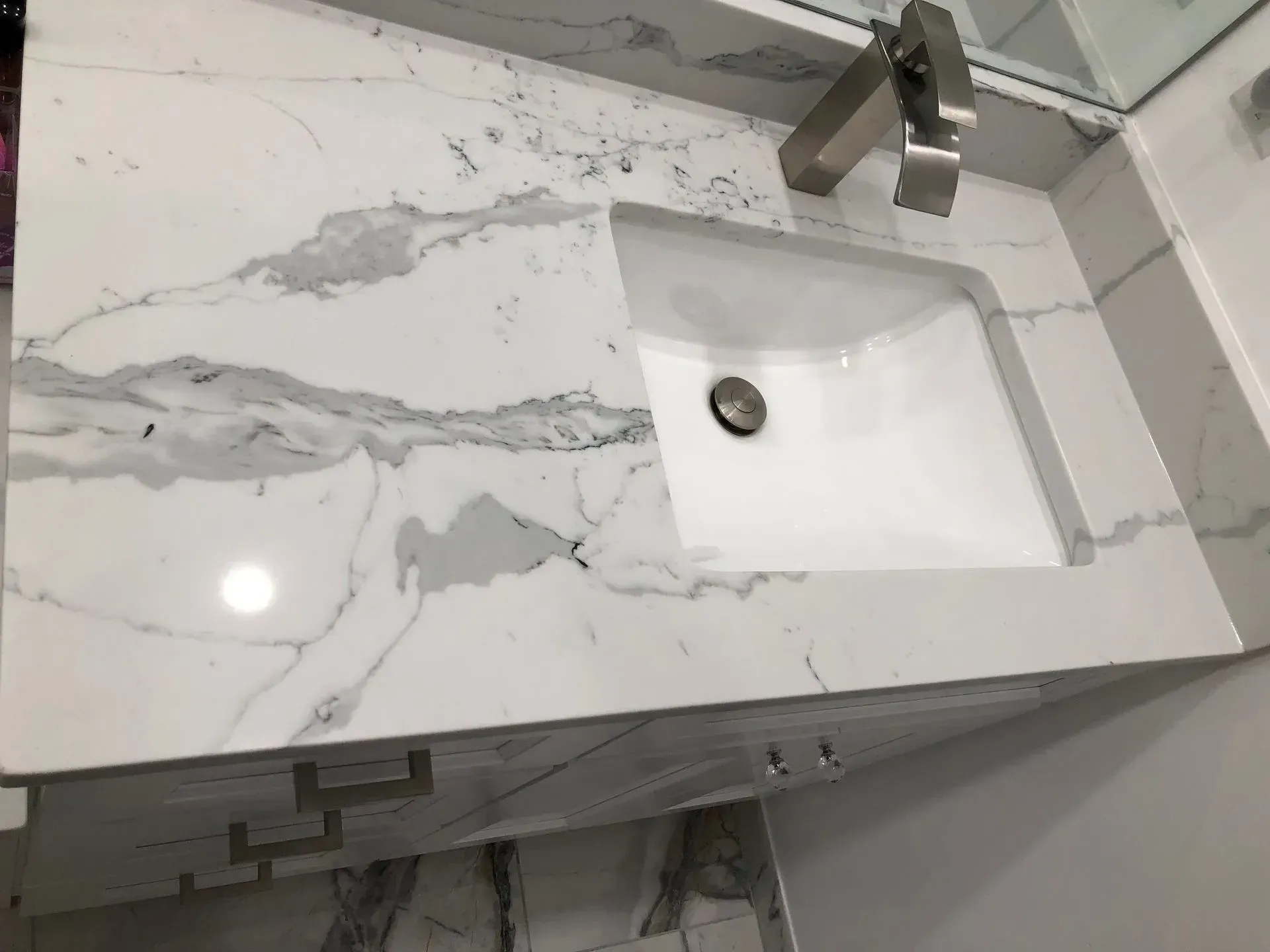 Modern bathroom vanity with white marble countertop, integrated sink, and wall-mounted faucet