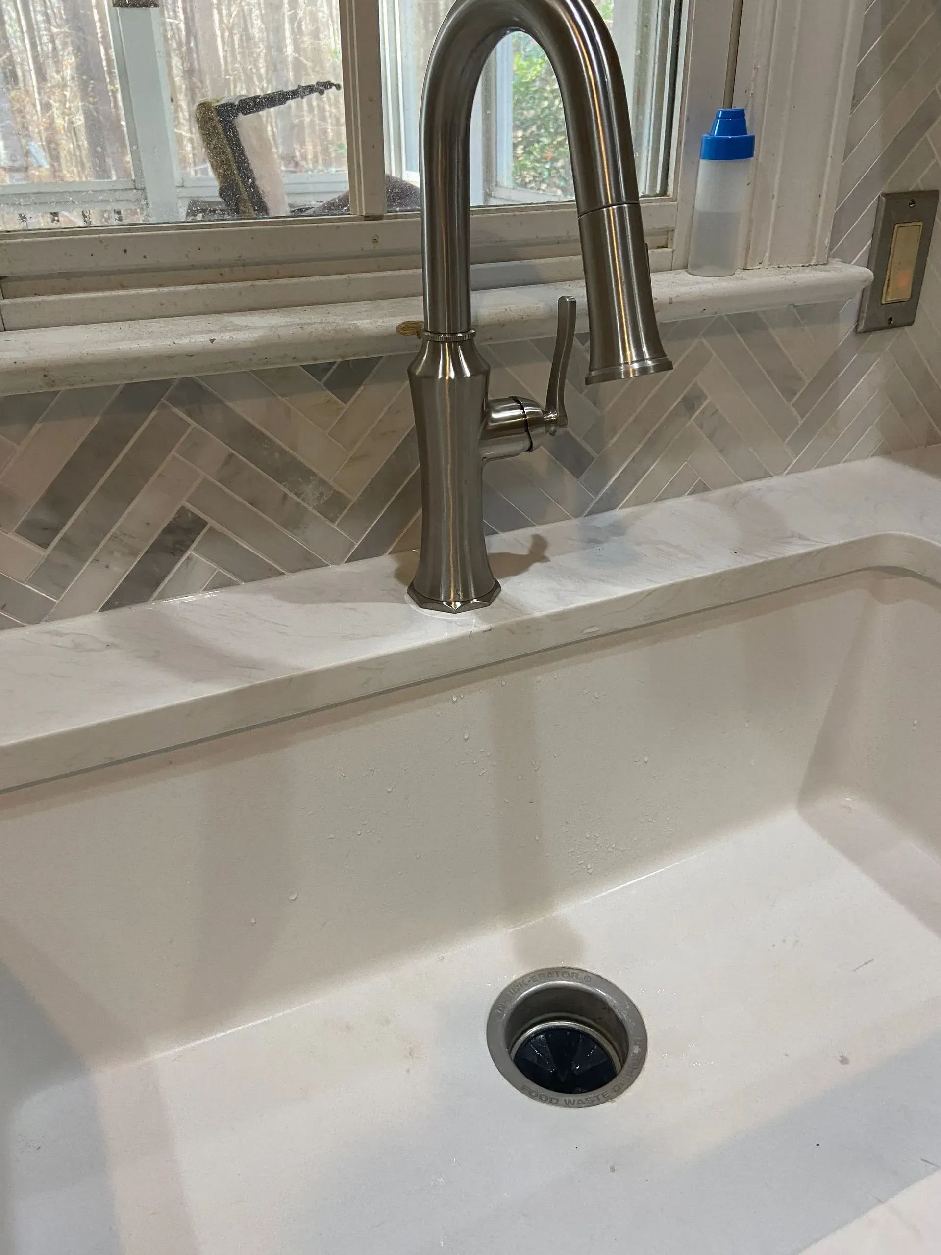 Bathroom sink with chrome faucet and soap dispenser on a countertop near a window.