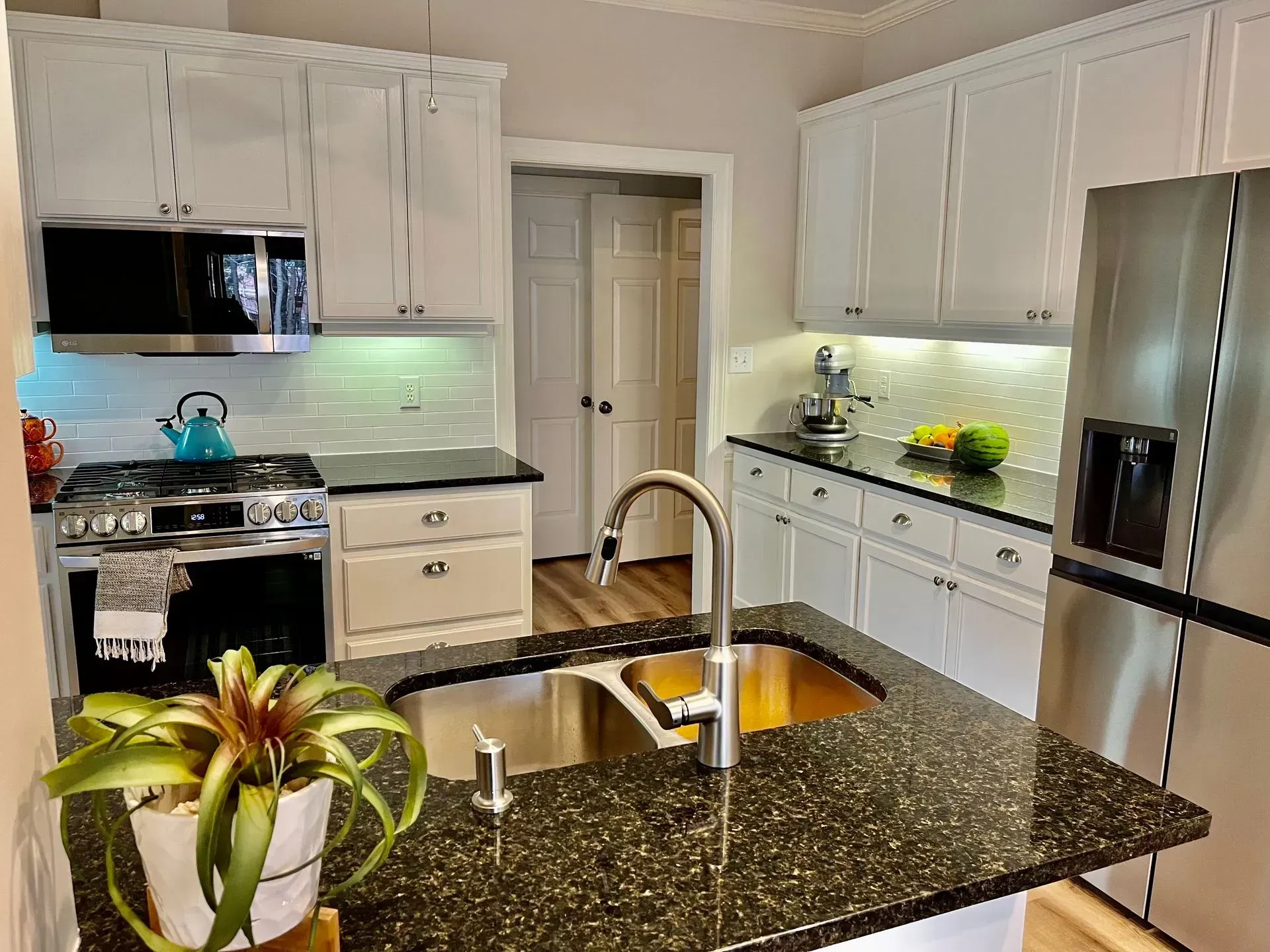 Bright modern kitchen with white cabinets, dark granite island, stainless steel appliances, and under-cabinet lighting