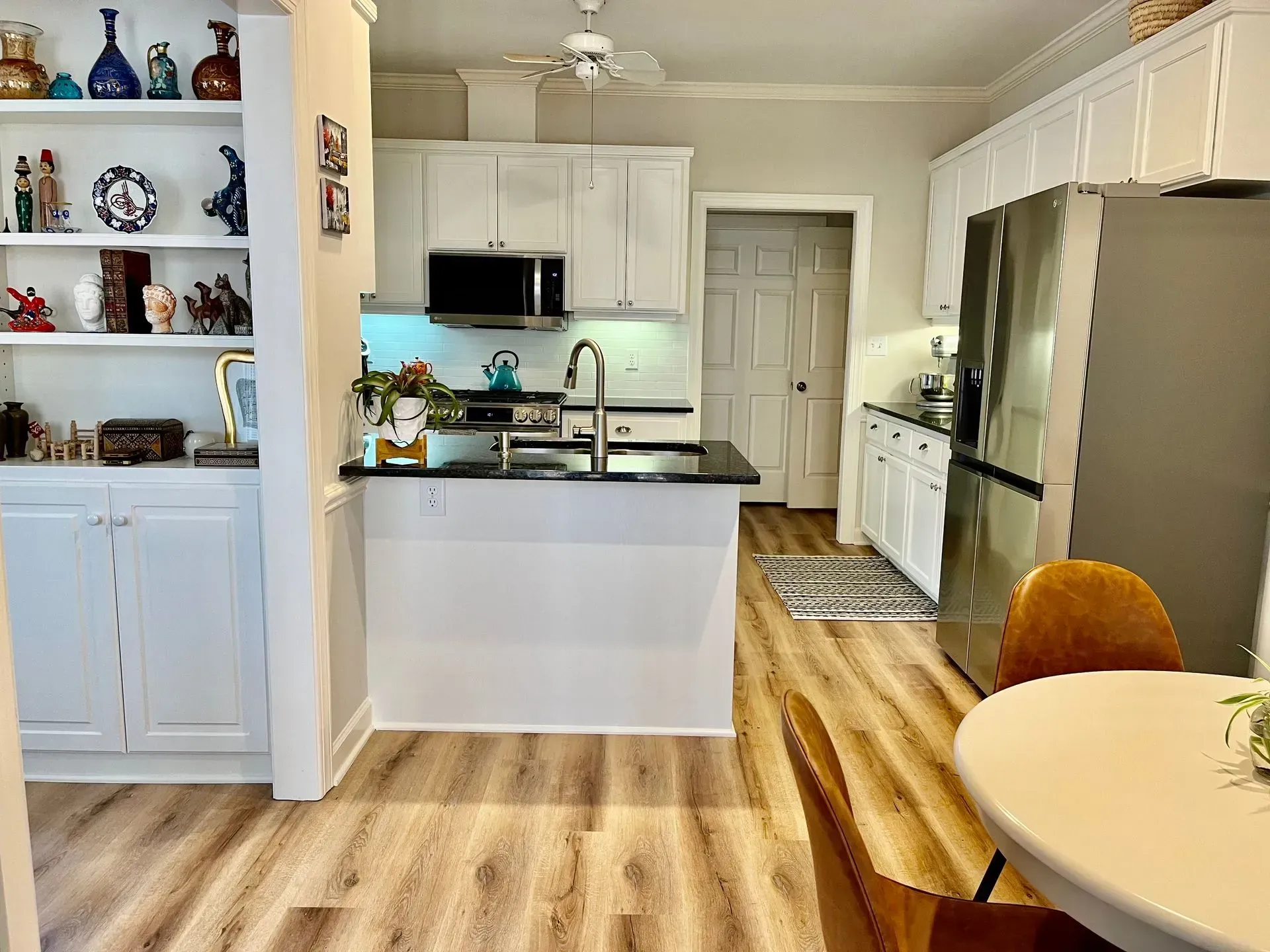 Bright kitchen with white cabinets, stainless fridge, black countertops, and hardwood floors, viewed from the dining area