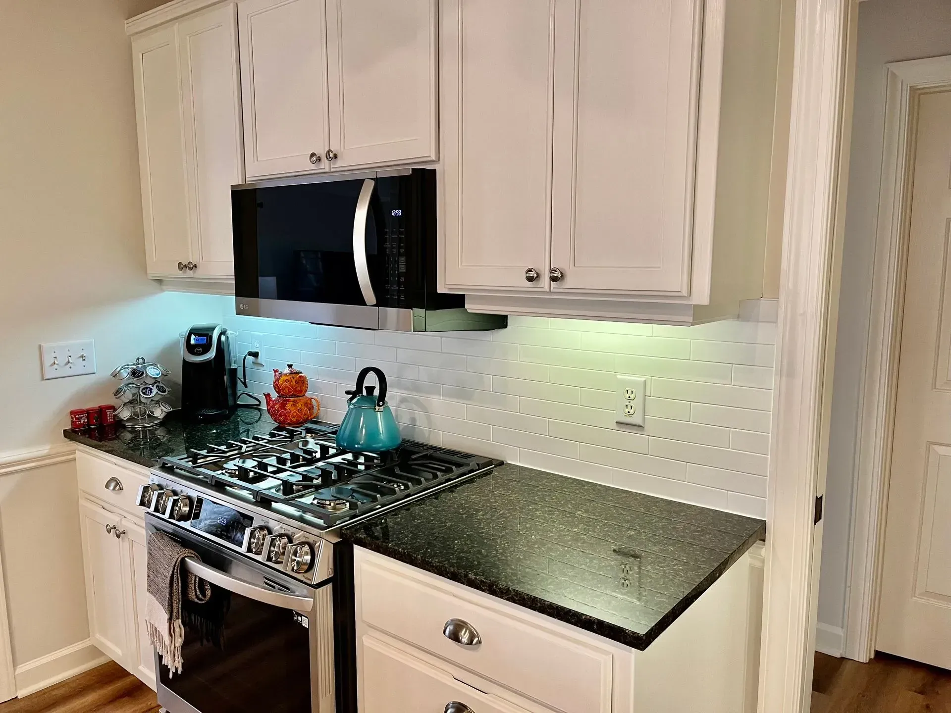 Modern kitchen with white cabinets, black countertop, stainless stove, and subway tile backsplash