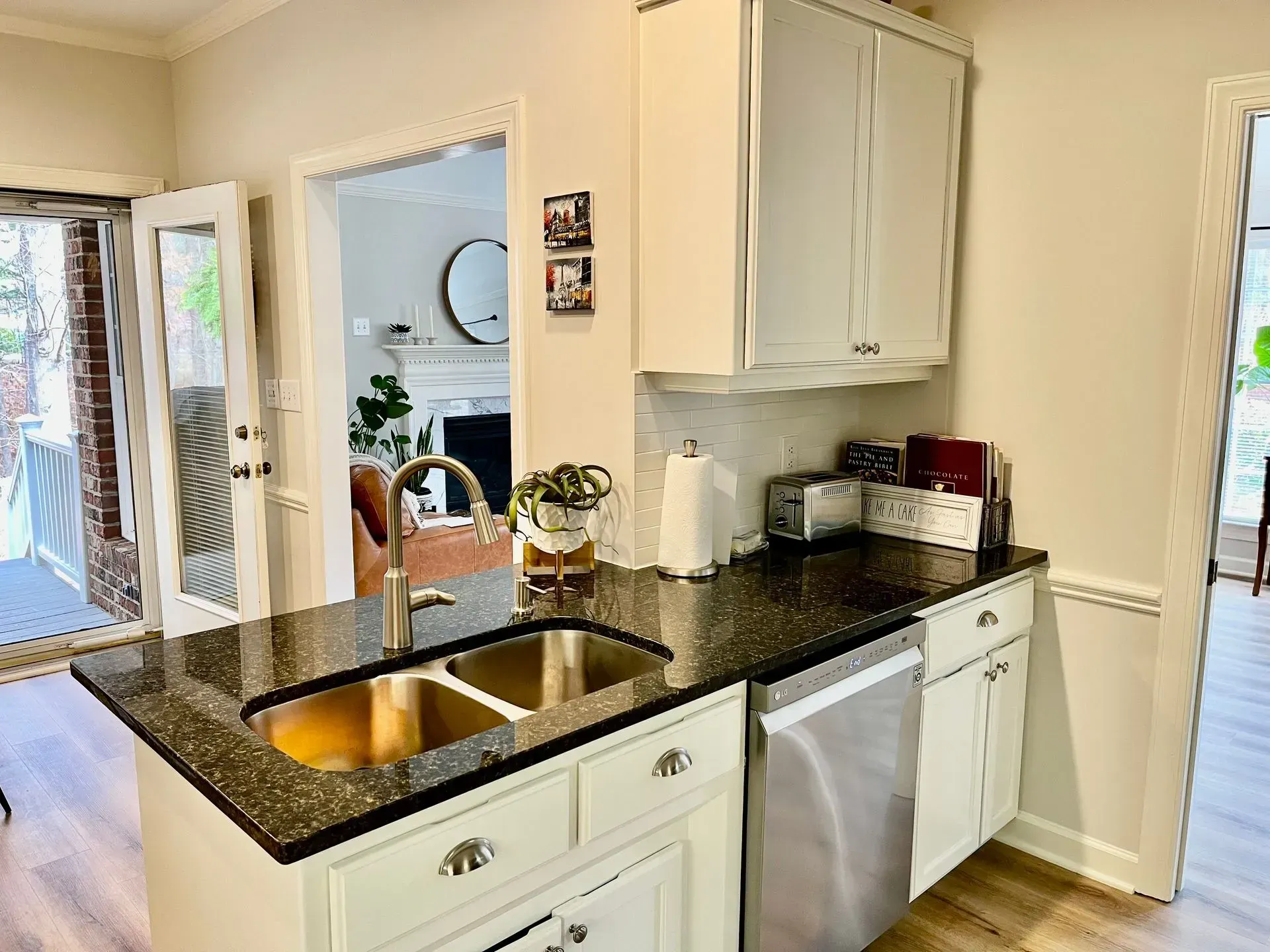 Bright kitchen with black granite counters, white cabinets, double sink, and stainless dishwasher.