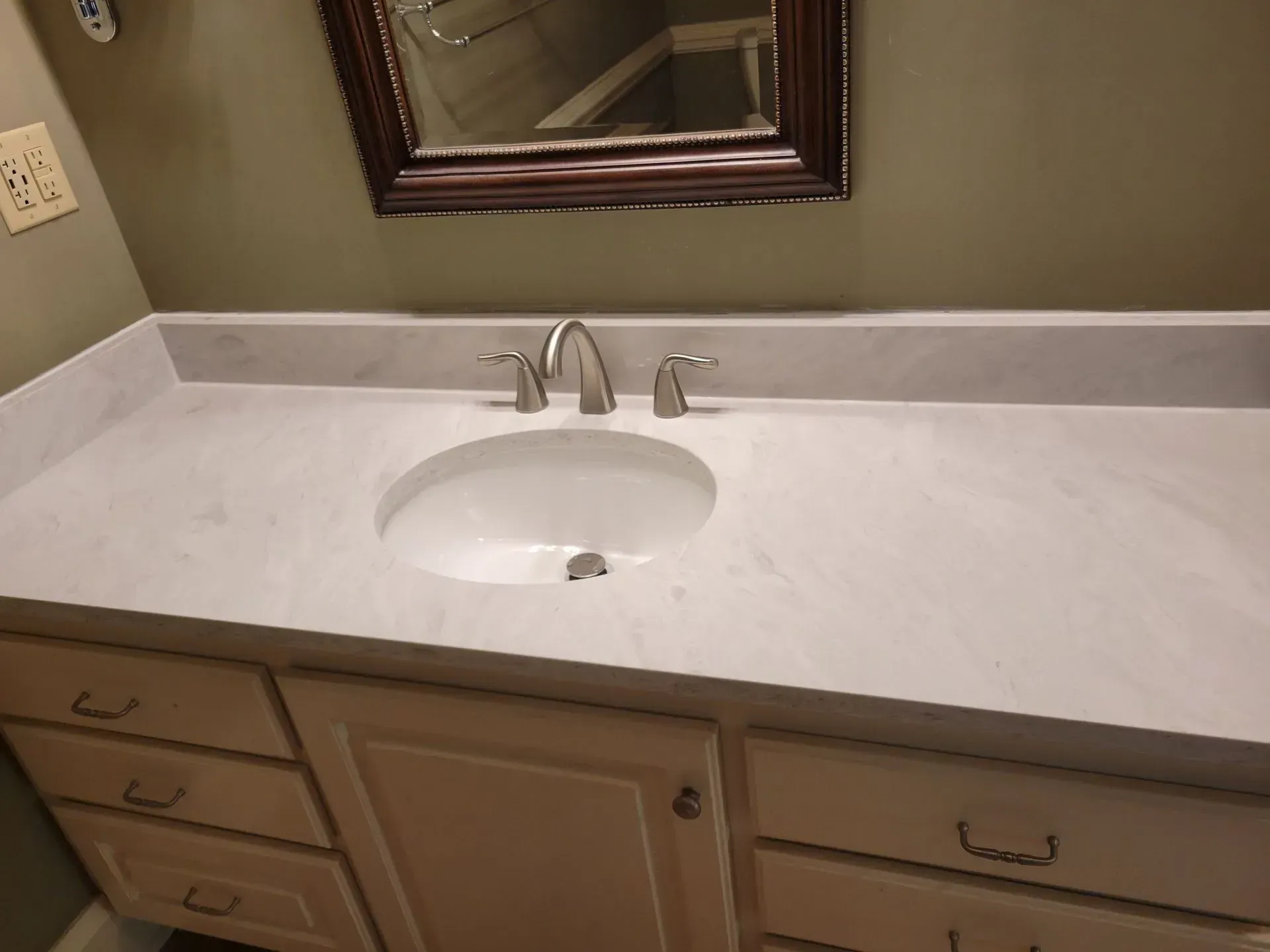Bathroom vanity with white countertop, built-in sink, chrome faucet, and mirror above wooden cabinets