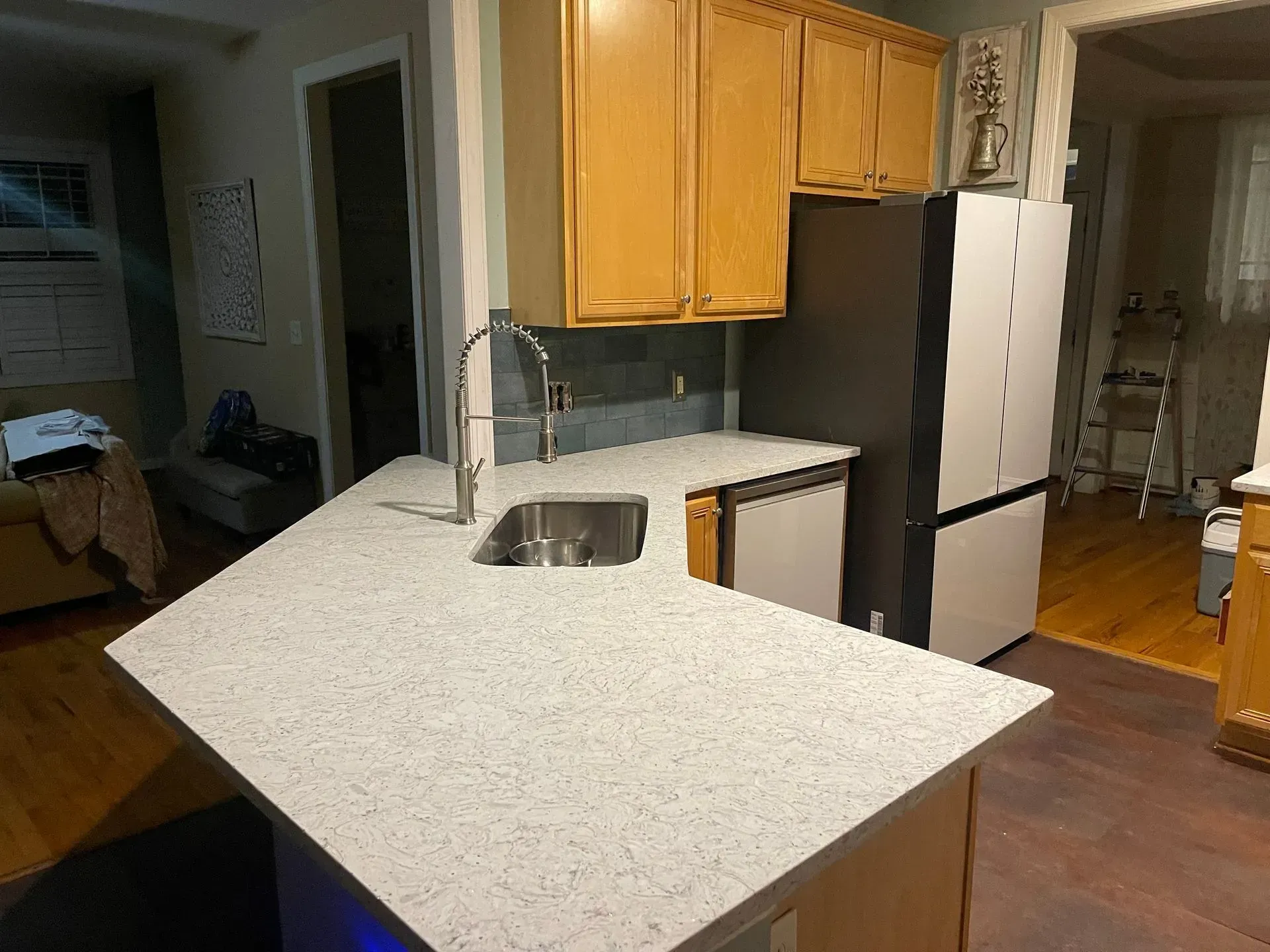 Kitchen with speckled island countertop, sink, wood cabinets, and white refrigerator.