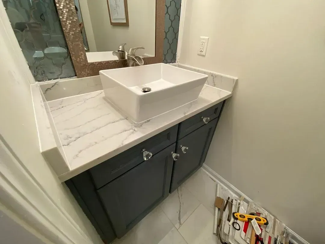 Modern bathroom vanity with white sink, dark cabinets, and marble countertop; tools on the floor.
