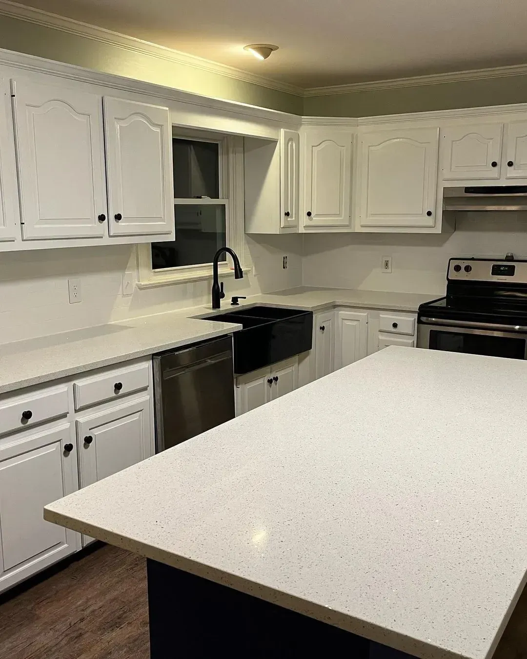 White kitchen with island, black appliances, and white cabinets around a sink and window.