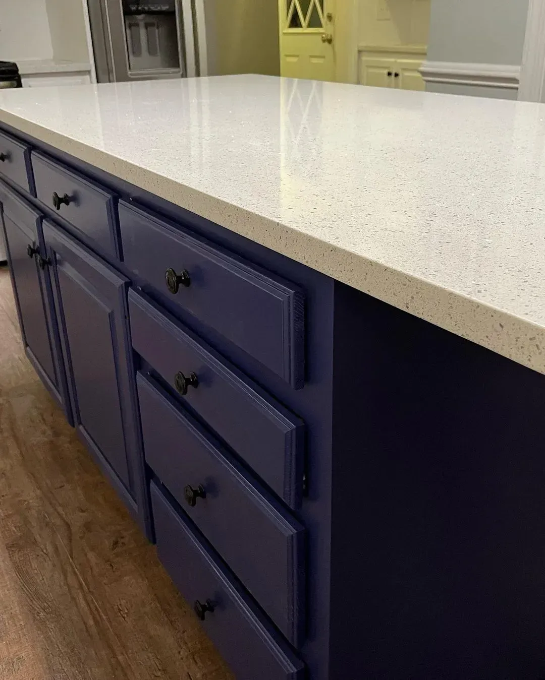 Blue kitchen island with white speckled countertop and wood floor.